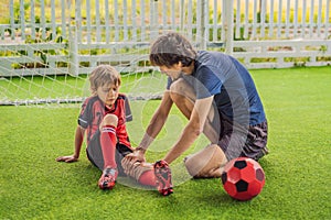Little cute kid boy in red football uniform and his trainer or father playing soccer, football on field, outdoors