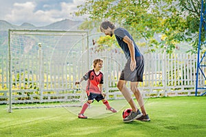 Little cute kid boy in red football uniform and his trainer or father playing soccer, football on field, outdoors