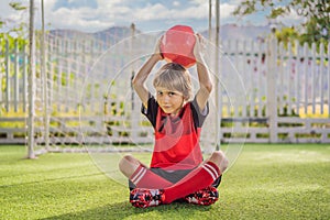 Little cute kid boy in red football uniform playing soccer, football on field, outdoors. Active child making sports with