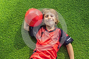 Little cute kid boy in red football uniform playing soccer, football on field, outdoors. Active child making sports with