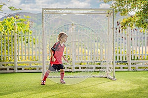 Little cute kid boy in red football uniform playing soccer, football on field, outdoors. Active child making sports with