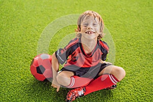 Little cute kid boy in red football uniform playing soccer, football on field, outdoors. Active child making sports with