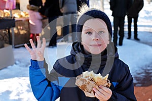 Little cute kid eats hot street food on Christmas market. Happy child on traditional family market in Europe