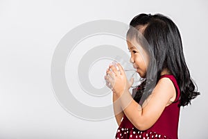 Little cute kid girl 3-4 years old smile drinking fresh water from glass in studio shot isolated