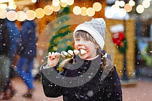 Little cute kid girl eating white chocolate covered strawberries on skewer on traditional German Christmas market. Happy