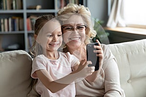 Little cute kid girl recording funny mobile video with granny.