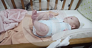 Little cute newborn baby lies on her back in the crib.