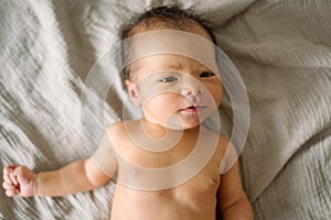 Little cute newborn smiling and laying in bed with soft natural light and naked. baby only days old looking in camera happy and