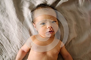 Little cute newborn smiling and laying in bed with soft natural light and naked. baby only days old looking in camera happy and