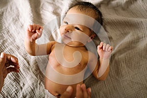 Little cute newborn smiling and laying in bed with soft natural light and naked. baby only days old looking in camera happy and