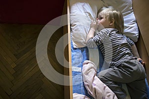 Little cute pensive blonde boy lying in bed