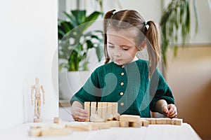 Little cute preschool girl plays at home with wood toys on table. Natural tactility development