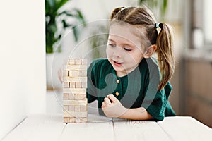 Little cute preschool girl plays at home with wood toys on table. Natural tactility development