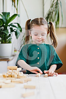 Little cute preschool girl plays at home with wood toys on table. Natural tactility development. Vertical orientation