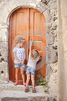 Little cute sisters near old door in Greek village