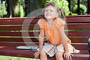 Little cute smiling girl with book on bench