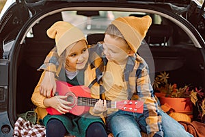 Little cute smiling girl and boy standing near by on open car trunk. Kid resting with her family in the nature. Autumn season