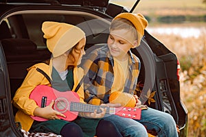 Little cute smiling girl and boy standing near by on open car trunk. Kid resting with her family in the nature. Autumn season