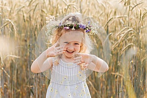 Little cute smiling girl with a wreath of flowers on her head in the summer in nature