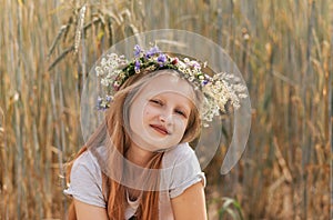 Little cute smiling girl with a wreath of flowers on her head in the summer in nature