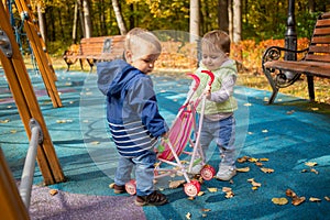 Little cute toddler boy and a beautiful year-old baby girl in blue clothes play in a pink toy stroller for a doll in the