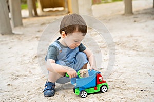 Little cute toddler boy 2.5 years old plays in the sandbox on a sunny summer day. Outdoor creative activities for kids. Toy car