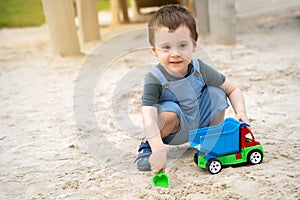 Little cute toddler boy 2.5 years old plays in the sandbox on a sunny summer day. Outdoor creative activities for kids. Toy car