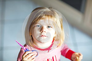 Little cute toddler girl making experiment with scissors and cutting hairs. Funny baby child cuts her pony herself at