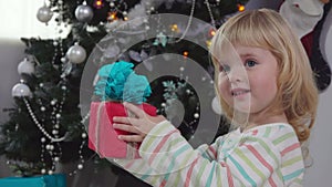 Little cute toddler girl in pajama is taking her gift box