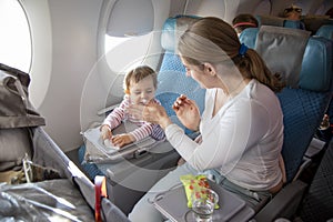 Little cute toddler girl sitting in an airplane in a chair by the porthole, holds a wet towel in her hands and sneezes