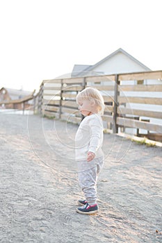 A little cute two-year-old girl in a light suit walks alone along the sandy path. Toddler proudly stands in the park, walk with