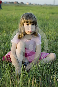 Little cute upset girl sitting in grass