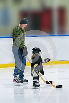 Little cute white hockey girl with dad on ice play hockey in full equipment