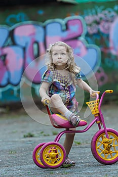 Little cyclist girl wearing checked tunic riding yellow and pink tricycle photo