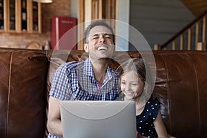 Little daughter and caring father watching funny video on laptop