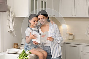 Little daughter congratulating mom in kitchen at home. Happy Mother`s Day