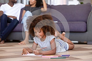 Little daughter drawing lying on floor parents sitting on couch