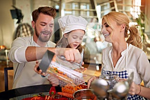 A little daughter enjoying to prepare a meal with her parents at home. Family, together, home