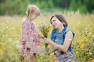 Little daughter gives her mother flowers. Mom and daughter walk in the summer nature. Mothers day, love and family concept