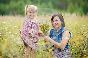 Little daughter gives her mother flowers. Mom and daughter walk in the summer nature. Mothers day, love, summer and family concept