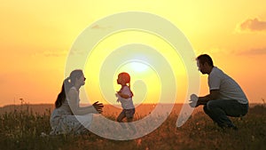 Little daughter goes from mom to dad, hugs and kisses her parents in rays of a warm sun. Happy family walks in park at