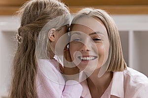 Little daughter kid whispering in mothers ear, sharing secret