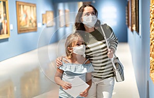 Little daughter and mother in protective masks inspect the exhibits in museum