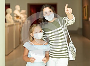 Little daughter and mother in protective masks inspect the exhibits in museum