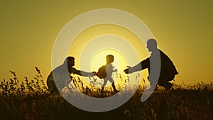 Little daughter with parents jumping at sunset. Silhouettes of mom dad and baby in the rays of dawn. Family concept