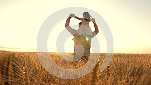 Little daughter plays on shoulders of farmers father in wheat field. Happy child and father are playing together in open