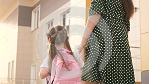 Little daughter schoolgirl walks with a backpack and holds her mother`s hand. preschool education concept. happy family