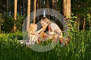 Little daughter shares apple with mom during a picnic in the park