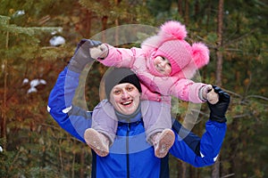 Little daughter sits on her father`s shoulders in the winter forest