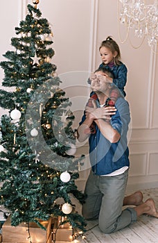 little daughter is sitting on dad's shoulders covering her eyes with her hands christmas tree decoration